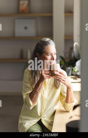 Zu Hause, reife Weiße, die den Becher hält und nach draußen blickt Stockfoto