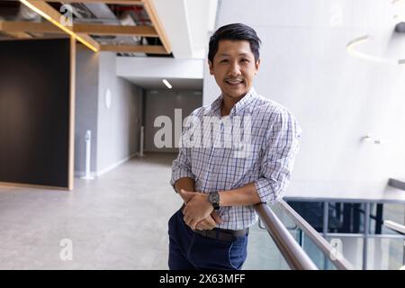 Asiatischer männlicher Profi, der allein im Büro steht und sich auf Geländer stützt Stockfoto