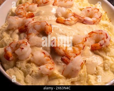 Eine Nahaufnahme eines Fischauflaufes, in dem die reichhaltige Konsistenz von Kartoffelpüree im Kontrast zu prallen Garnelen in einem cremigen Weißwein präsentiert wird Stockfoto