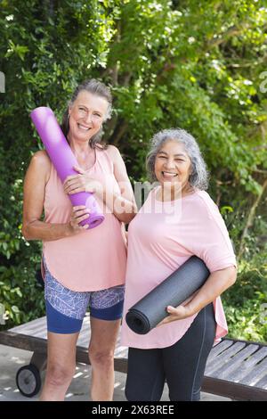 Draußen, verschiedene ältere Freundinnen, die Yogamatten halten, lächeln Stockfoto