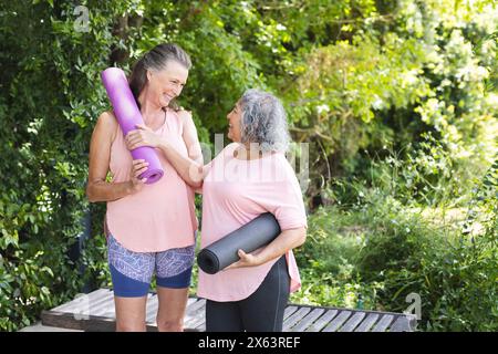 Verschiedene ältere Freundinnen, die draußen lächeln, Yogamatten tragen Stockfoto