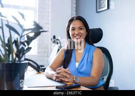 Im Büro eine Geschäftsfrau mit blauem Oberteil, die in die Kamera lächelt Stockfoto