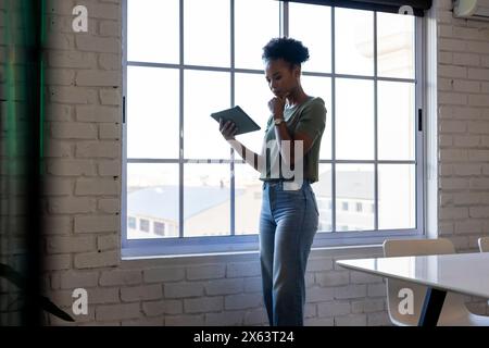 Im Büro steht eine afroamerikanische Geschäftsfrau, die auf ein Tablet blickt Stockfoto