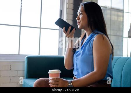 Im Büro, eine Geschäftsfrau, die ein Smartphone hält und wegschaut Stockfoto
