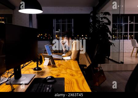 Im Büro, eine afroamerikanische Geschäftsfrau, die bis spät an einem Laptop arbeitet Stockfoto