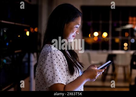 Im Büro, Geschäftsfrau mit birassischem Smartphone, die bis spät arbeitet Stockfoto
