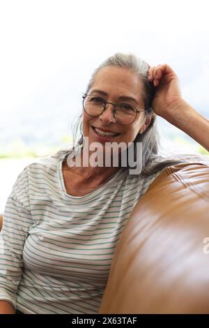 Zu Hause sitzt eine kaukasische reife Frau mit Brille und lächelt Stockfoto