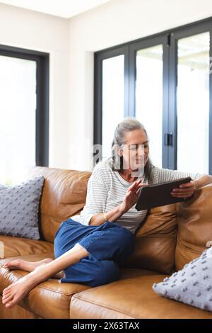 Zu Hause, reife kaukasische Frau, die auf dem Sofa sitzt und auf ein Tablet blickt Stockfoto
