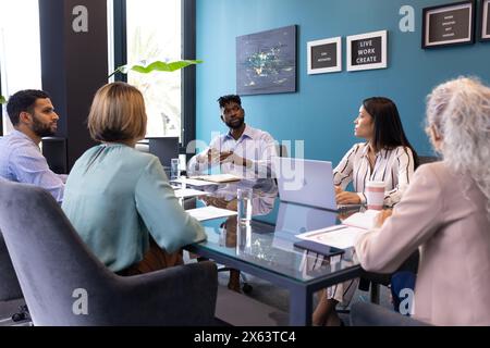 Ein vielseitiges Team diskutiert am Tisch im Büro, ein ranghöchster afroamerikanischer Mann führt Stockfoto