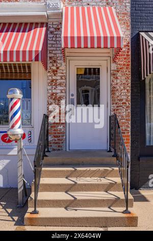 Princeton, IL, USA-28. Februar 2024: Vordereingang zum altmodischen, kleinen Stadtfriseur mit hellrot gestreiftem Markise und klassischer Friseurstange. Stockfoto