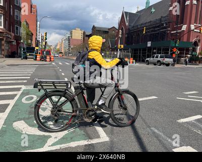 E-Bike-Fahrer-Lieferer warten auf die Ampel, die an der 4th Avenue und 9th Street im Park Slope Abschnitt von Brooklyn, New York, grün wird. Stockfoto