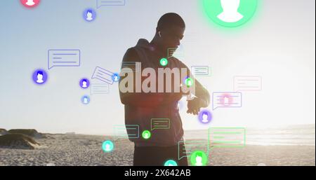 Bild von mehreren Symbolen, afroamerikaner, der Kopfhörer anpasst und Smartwatch betrachtet Stockfoto