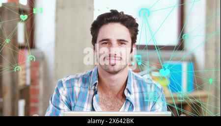 Bild von verbundenen Ikonen, die sich über dem kaukasischen Mann befinden, der im Büro am Laptop arbeitet Stockfoto