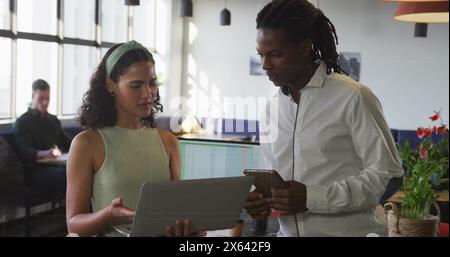 Bild einer birassischen Frau mit Laptop spricht mit afroamerikanischem Mann auf Smartphone Stockfoto