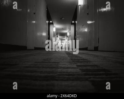 Dunkler, geheimnisvoller Flur im Hotelgebäude, Niedrigwinkelaufnahme. Blick auf das Türzimmer in einem einsamen, ruhigen Apartment mit Licht auf schwarz-weißem Stall Stockfoto