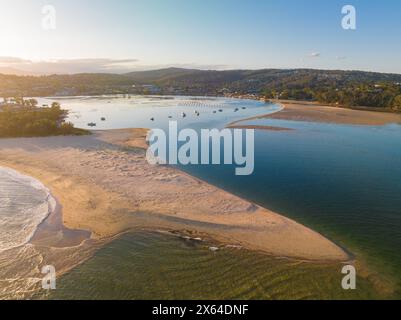 Blick aus der Vogelperspektive auf den Sonnenuntergang über einer Küste mit einer langen vorstehenden Sandbank bei Merimbula in New South Wales, Australien Stockfoto