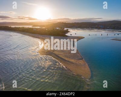 Blick aus der Vogelperspektive auf den Sonnenuntergang über einer Küste mit einer langen vorstehenden Sandbank bei Merimbula in New South Wales, Australien Stockfoto