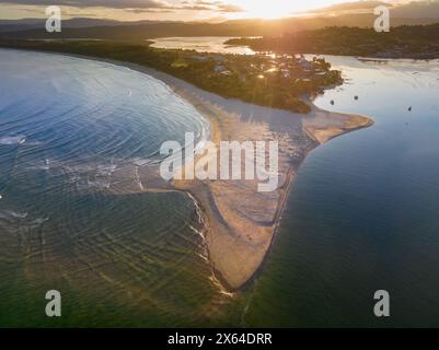 Blick aus der Vogelperspektive auf den Sonnenuntergang über einer Küste mit einer langen vorstehenden Sandbank bei Merimbula in New South Wales, Australien Stockfoto