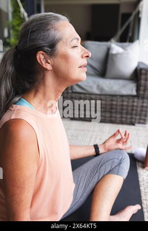 Zu Hause, reife kaukasische Frau mit grauem Haar, die meditiert und drinnen Yoga macht Stockfoto