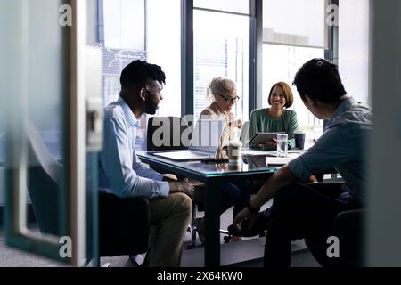 Verschiedene Teams diskutieren am Tisch im Büro, schauen sich einen Laptop an Stockfoto