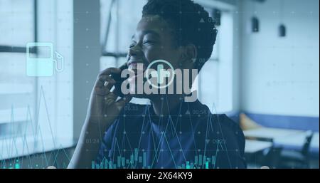 Bild von Ikonen, Diagrammen und wechselnden Zahlen, lächelnde afroamerikanerin, die auf dem Handy spricht Stockfoto