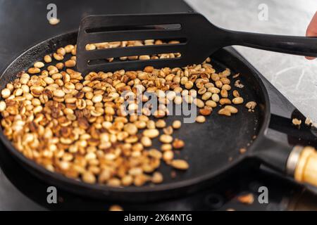 Kaffeebohnen werden in einer gusseisernen Pfanne geröstet. Grüne Körner werden mit einem Teigschaber vermischt. Ausgewählter Fokus. Hochwertige Fotos Stockfoto