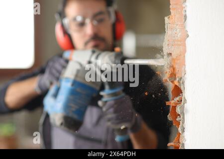 Bauarbeiter, der mit einem Bohrhammer eine Wand in einem Haus zerstört Stockfoto