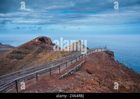 Eine felsige Klippe überblickt das Meer mit einem Zaun, der zum Wasser führt. Die Szene ist ruhig und friedlich, mit dem Geräusch von Wellen, die im Hintergrund zusammenbrechen Stockfoto