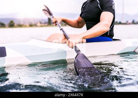 Kanufahrer, der im Kanu sitzt und Paddel hält, im Wasser. Das Konzept des Kanufahrens als dynamischer und abenteuerlicher Sport. Rückansicht, Sportmann mit Blick auf das Wasser Stockfoto