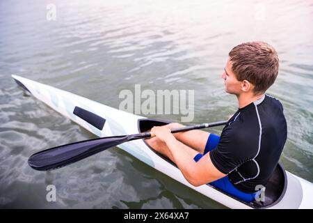 Kanufahrer, der im Kanu sitzt und Paddel hält, im Wasser. Das Konzept des Kanufahrens als dynamischer und abenteuerlicher Sport. Rückansicht, Sportmann mit Blick auf das Wasser Stockfoto