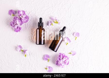 Draufsicht auf Kosmetikflaschen aus dunklem Glas mit einer Pipette mit einem natürlichen Gesichtspflegeprodukt. . Flache Lagen. Weißer Hintergrund, Blumen Stockfoto