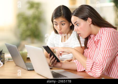 Zwei verblüffte Tele-Mitarbeiter, die zu Hause Telefoninhalte anschauen Stockfoto