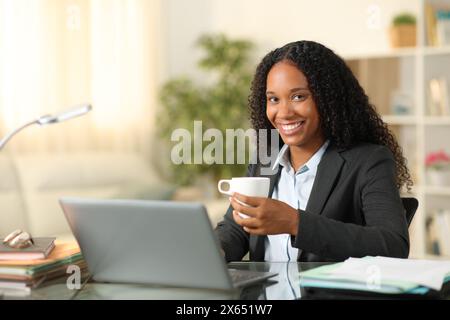 Ein glücklicher Telearbeiter posiert mit einer Kaffeetasse zu Hause und blickt in die Kamera Stockfoto