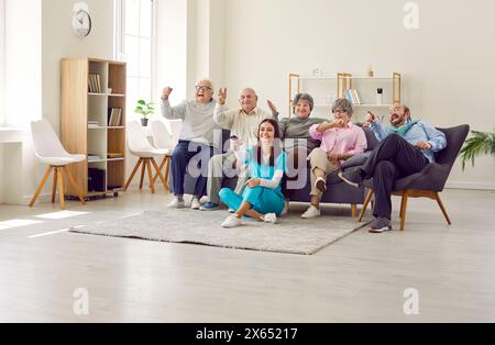 Gruppe von Senioren, die im Altersheim fernschauen, mit einer jungen Krankenschwester in der Ferne. Stockfoto