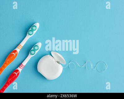 Zwei Zahnbürste und eine Schachtel Zahnseide auf blauem Hintergrund. Zahngesundheit und tägliche Zahnpflege-Routinekonzept. Stockfoto