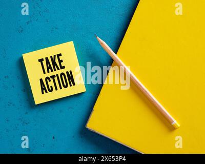 Das Wort Take Action auf gelbem Haftnotizpapier mit Bleistift und Bindemittel. Stockfoto