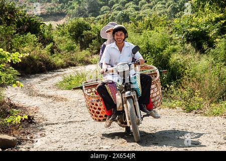 Ein asiatisches Paar fährt mit einem Motorrad zurück nach Hause von einer Stadt in ihr Bergdorf. Ein Motorrad, das mit Korbkörben beladen ist Stockfoto