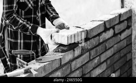 Eine junge Maurerin baut eine Mauer, legt einen Ziegel auf einen Zementmörtel Stockfoto