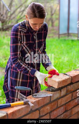Eine junge Maurerin baut eine Mauer, legt einen Ziegel auf einen Zementmörtel Stockfoto