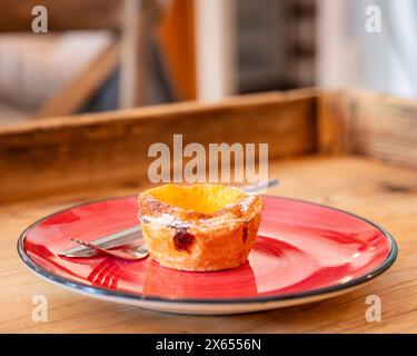 Eine Pastel de Nata oder portugiesische Eiertorte. Traditionelle Pastell de Nata Pustard Tarte auf einem roten Teller mit Messer und Gabel. Stockfoto