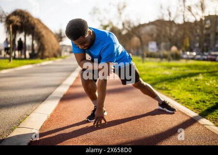 Ein junger afroamerikanischer Mann übt in der Stadt aus. Er dehnt seinen Körper aus. Stockfoto