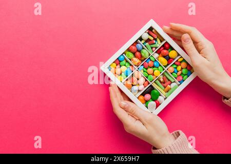 Weibliche Hände mit köstlichen Süßigkeiten in der Schachtel auf farbigem Hintergrund. Stockfoto