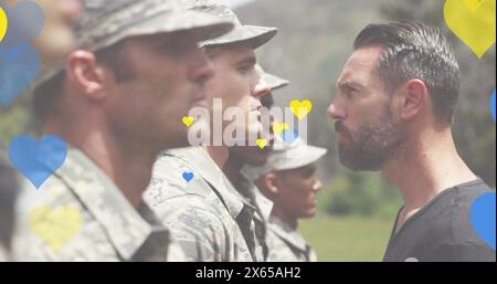 Bild von gelben und blauen Herzen, die über verschiedene männliche Soldaten und Trainer schweben Stockfoto