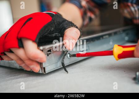 Detaillierte Nahaufnahme der Hand des Technikers in rotem Handschuh mit gelbem Schraubendreher zum Festziehen der Schraube an der Metallvorrichtung, die präzise mechanische Arbeit demonstriert. Stockfoto