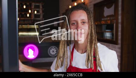 Junger, birassischer Mann mit roter Schürze, der ein digitales Tablet in einem Café hält Stockfoto