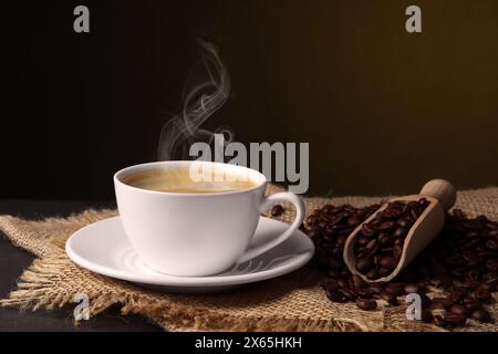 Dampfgaren von Kaffee in der Tasse und gerösteten Bohnen auf dem Tisch Stockfoto