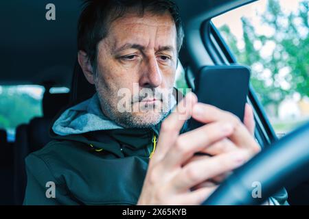Männlicher Fahrer mit Smartphone-Gerät im Auto, selektiver Fokus Stockfoto