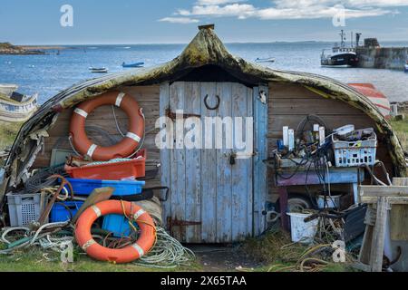 Umgedrehtes Fischerboot, das in einen alten Schuppen mit Ausrüstung umgebaut wurde, das auf der Heiligen Insel verstreut ist. Stockfoto