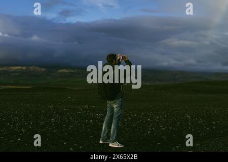 Ein Reisender mit Rucksack in Island macht Fotos mit seinem Handy. Stockfoto