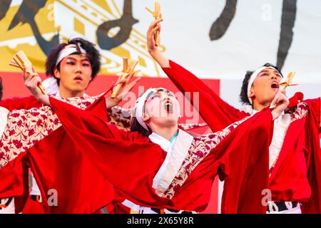 Japanische Teenager-Frau Yosakoi-Tänzerin in rotem, langärmligen Yukata tanzt auf der Bühne mit Naruko, Holzklatschen, im Kyusyu Gassai in Kumamoto. Stockfoto